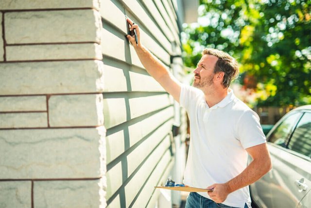 Person inspecting light gray commercial siding installation, holding a clipboard.